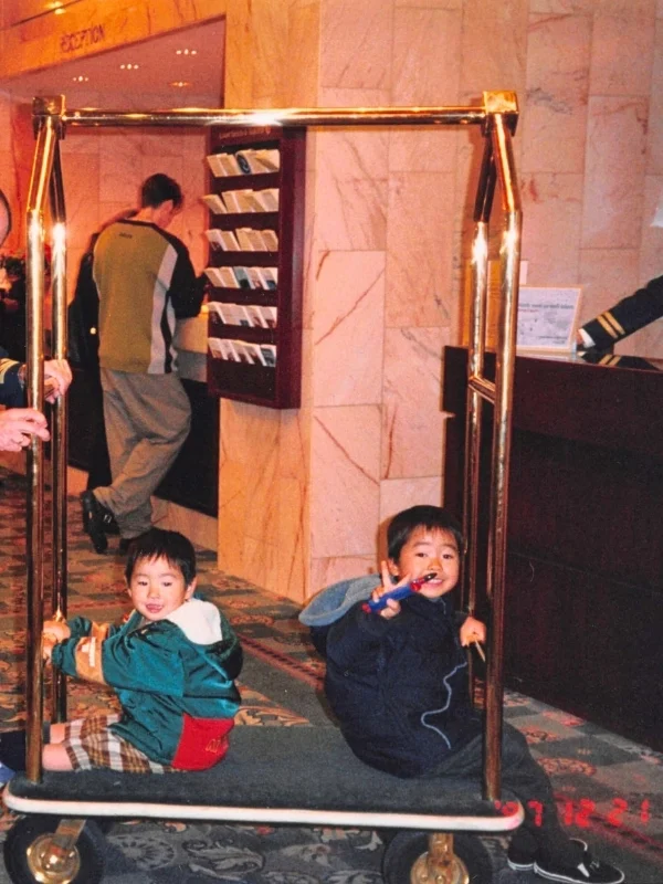 1997年12月、子連れでカナダに最初に滞在したホテルのロビーにある荷物カートに乗って遊ぶ2人の幼い息子。